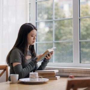Young asian woman sitting by the window and reading a book