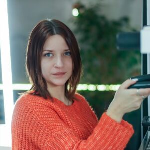 Young barista in orange sweater working at coffee machine counter